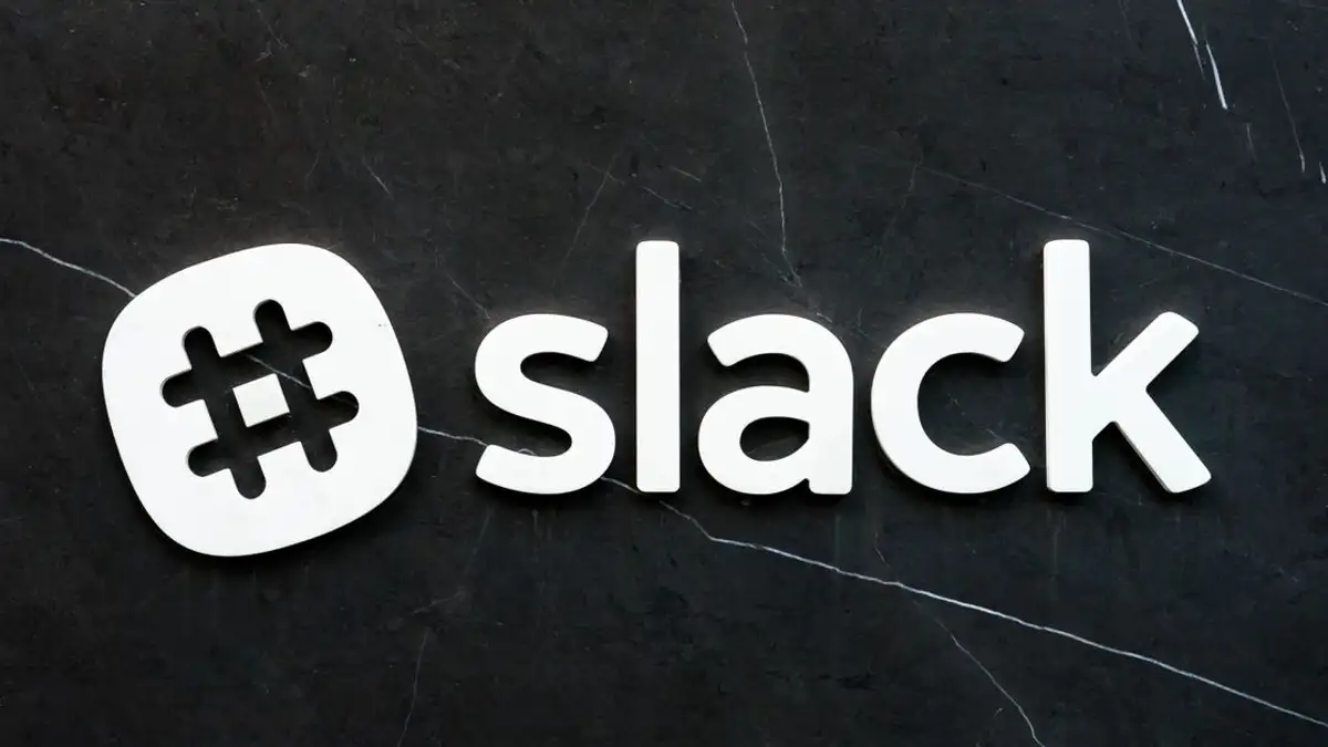 Close-up logo Slack dengan simbol hashtag di latar belakang tekstur gelap, menekankan komunikasi digital.