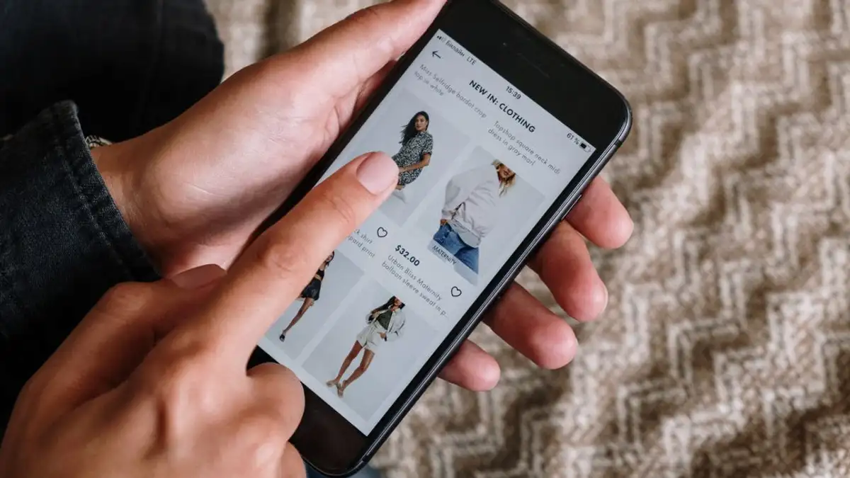 Orang yang menjelajahi barang pakaian di smartphone, menampilkan pengalaman belanja online modern.