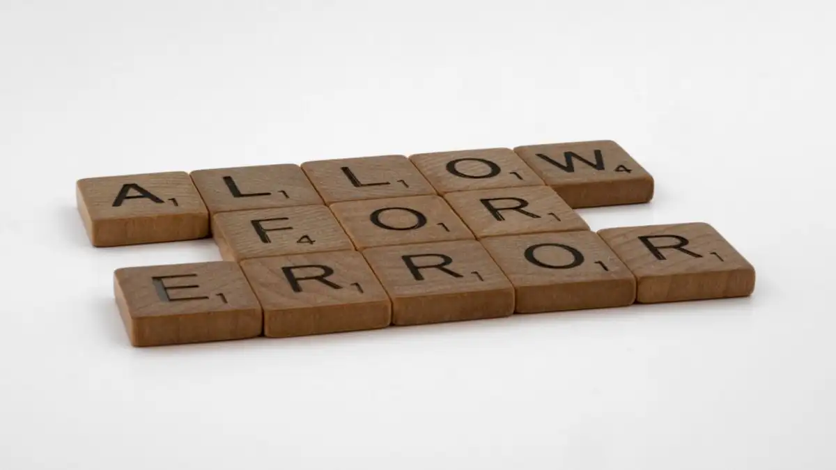 Bidak Scrabble yang mengeja 'Allow For Error' di latar belakang putih, melambangkan fleksibilitas dan penerimaan.