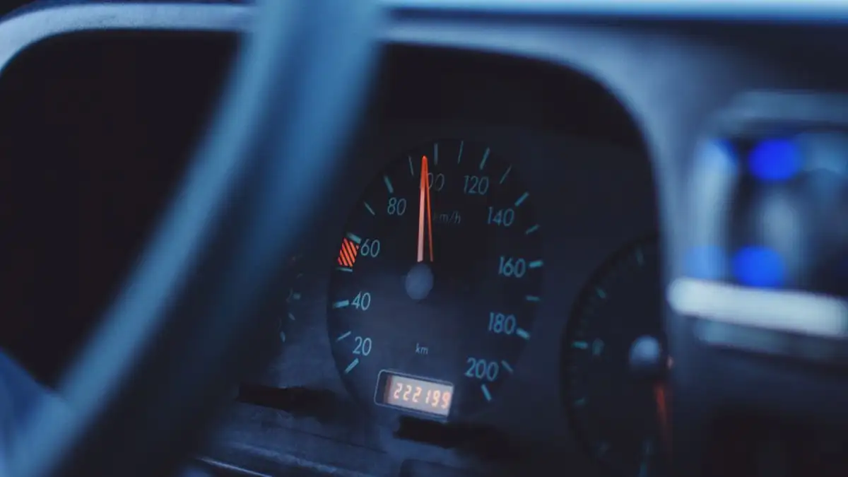 Gambar fokus dari speedometer dan tachometer mobil di bawah pencahayaan redup, menunjukkan jarak tempuh dan kecepatan.