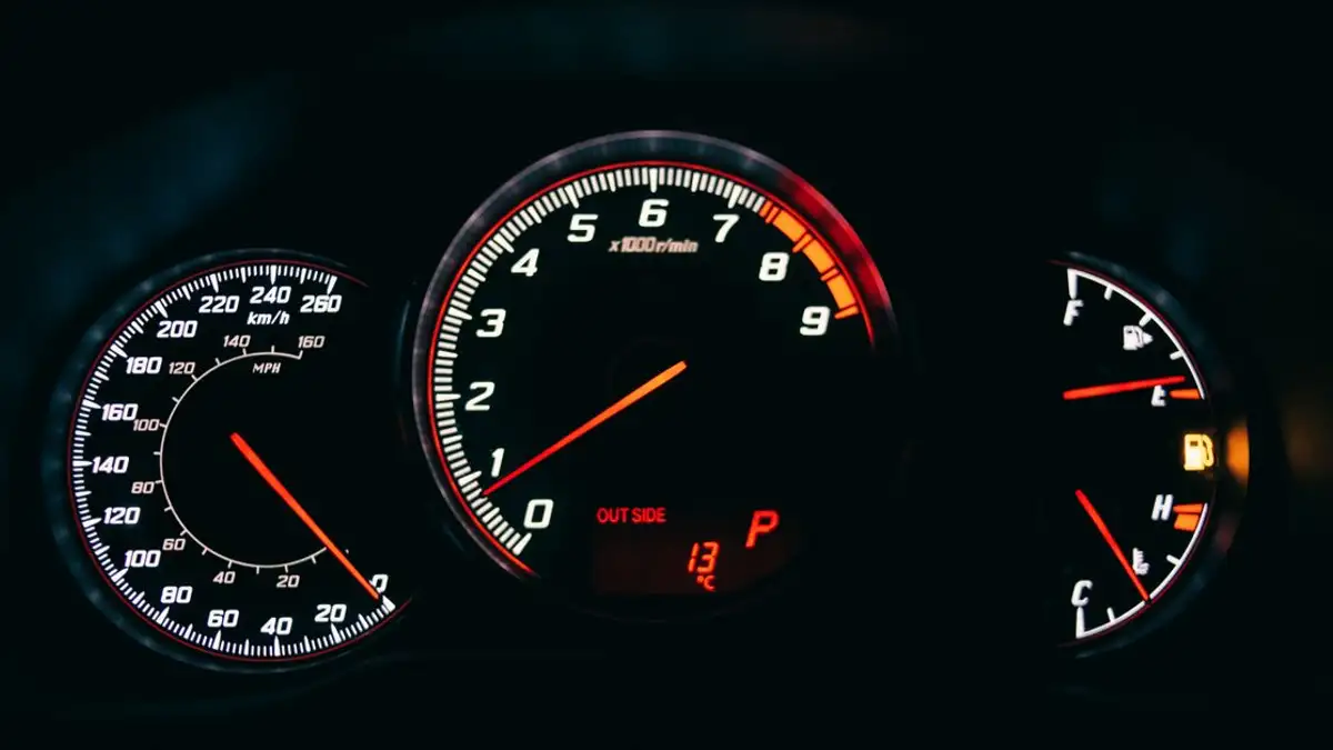 Kedekatan dasbor mobil yang menunjukkan speedometer dan pengukur dengan dial yang menyala di latar belakang hitam.