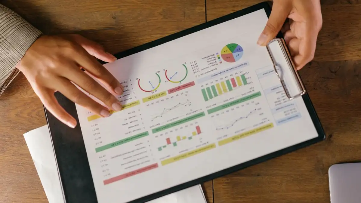 Pandangan atas tangan yang memegang laporan keuangan dengan grafik dan diagram berwarna, ideal untuk presentasi bisnis.