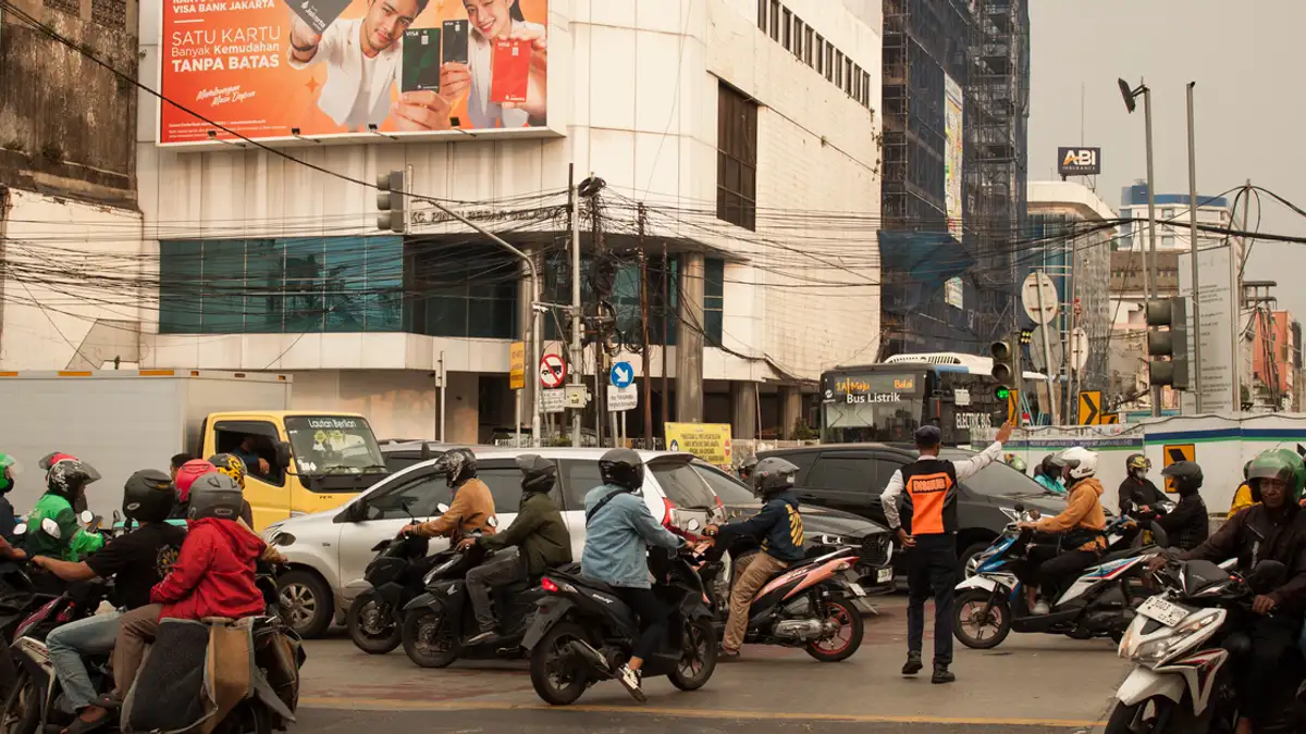 Sebuah pemandangan kota yang ramai di Jakarta dengan pengendara motor di persimpangan yang sibuk.