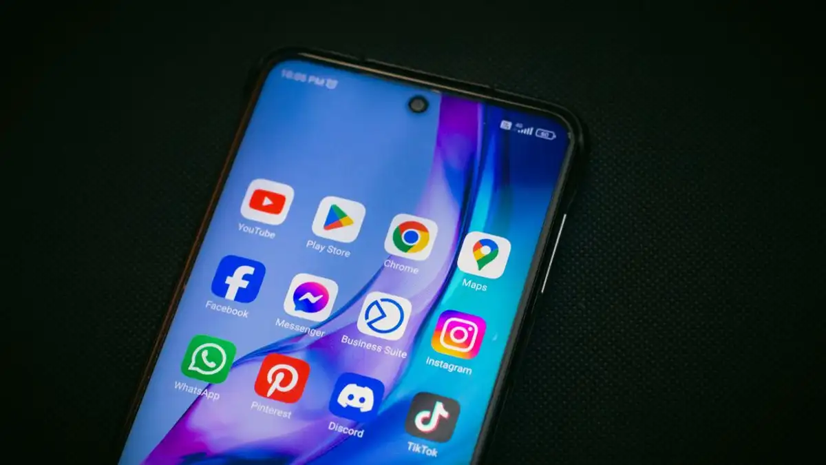 Close-up layar smartphone yang menunjukkan ikon aplikasi populer seperti YouTube, Peta, dan TikTok di latar belakang hitam.