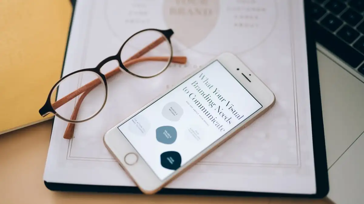 Close-up kacamata dan smartphone di atas dokumen tentang branding visual, sempurna untuk konsep bisnis.