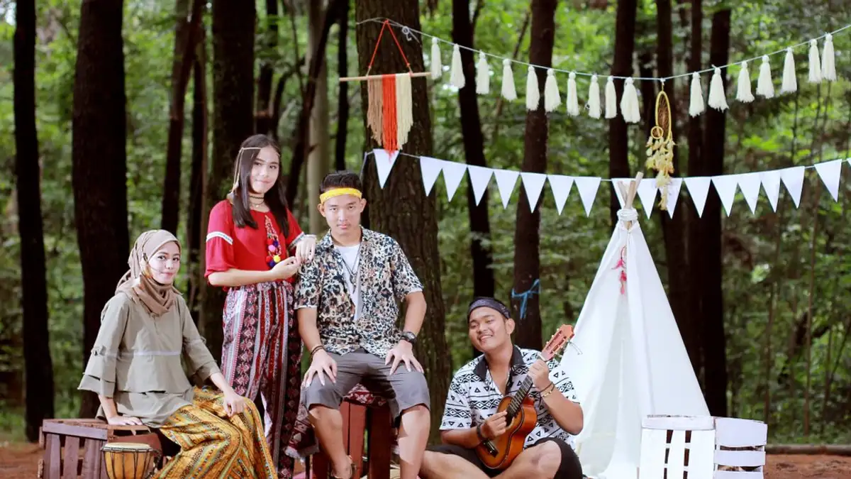 Sekelompok teman trendi menikmati perkemahan bergaya bohemian di hutan Indonesia.