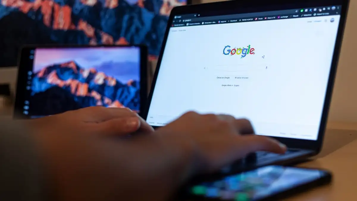 Tangan yang mengetik di laptop dengan Google di layar, dalam pengaturan kerja jarak jauh di Milan, Italia.