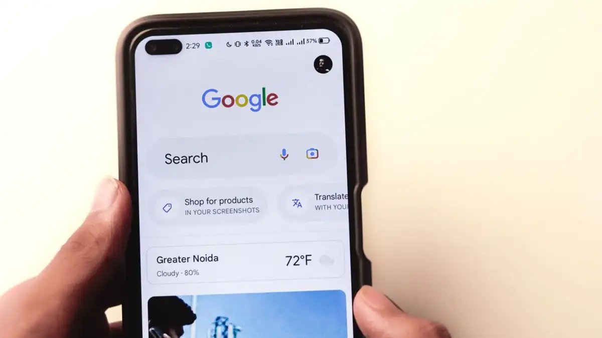 Close-up tangan yang memegang smartphone dengan pencarian Google ditampilkan di layar.