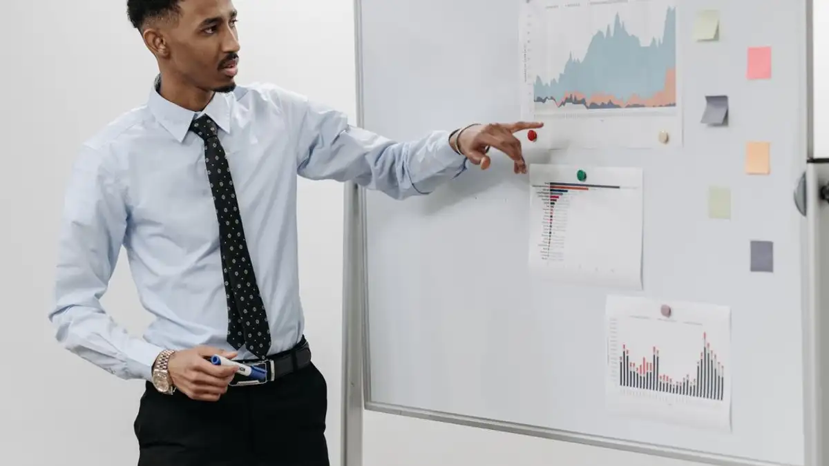 Pria mempresentasikan data bisnis dengan grafik di papan putih dalam sebuah pertemuan.