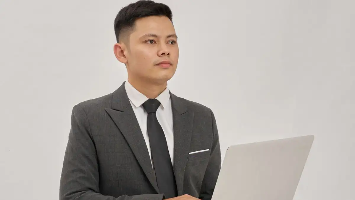 Profesional bisnis yang percaya diri mengenakan setelan jas menggunakan laptop di dalam ruangan yang terang.