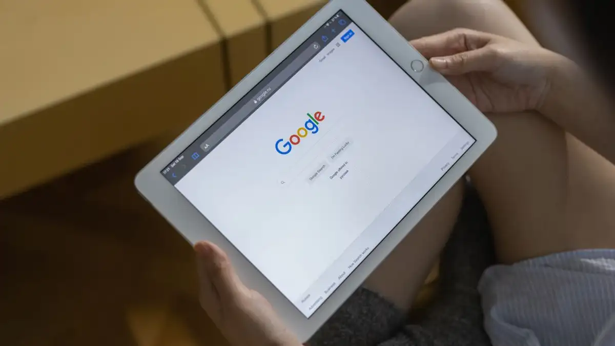 Close-up tangan memegang tablet yang menampilkan halaman pencarian Google.