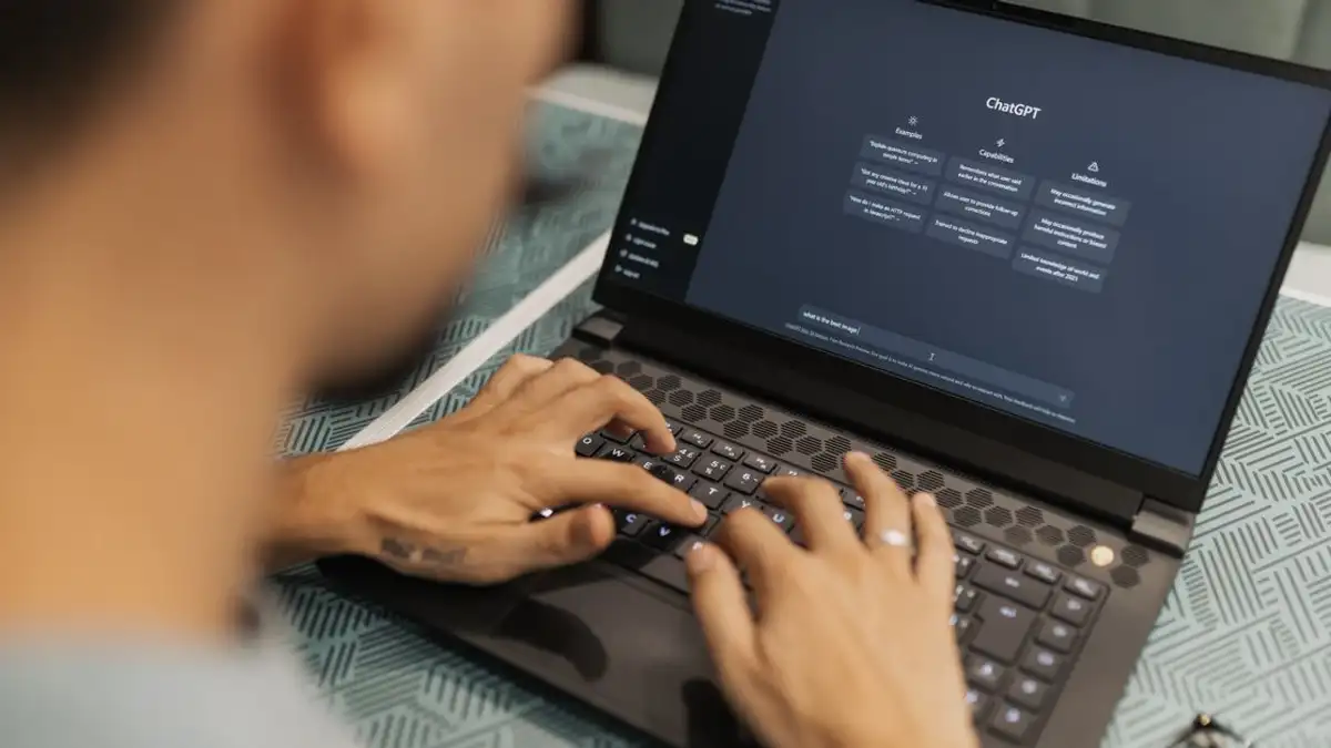 Seseorang yang fokus mengetik di laptop yang menjalankan perangkat lunak AI di dalam ruangan.