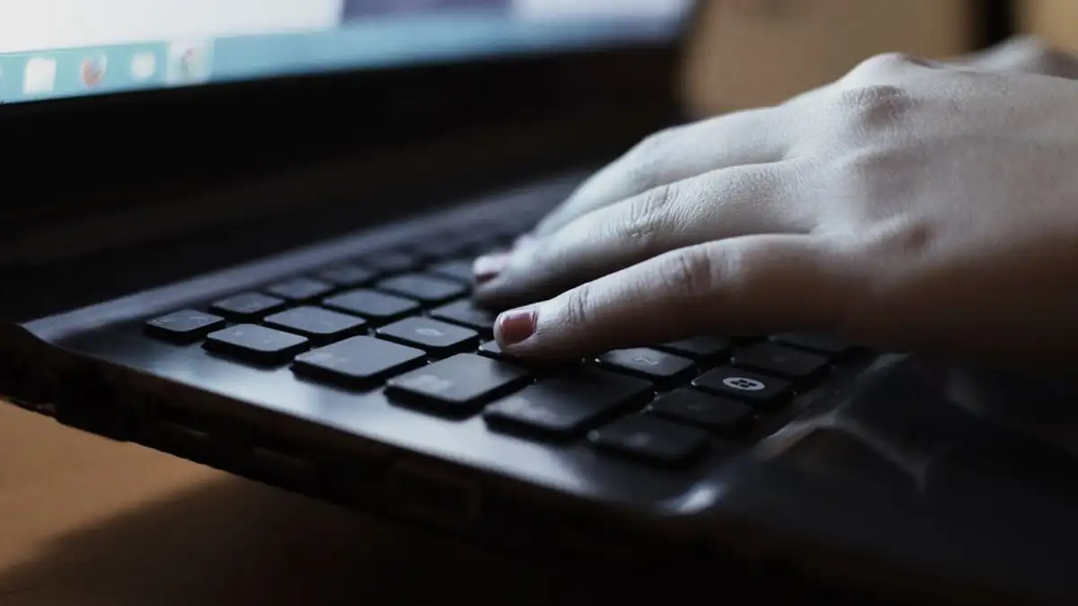 Tampilan close-up seseorang yang sedang mengetik di keyboard laptop di dalam ruangan.