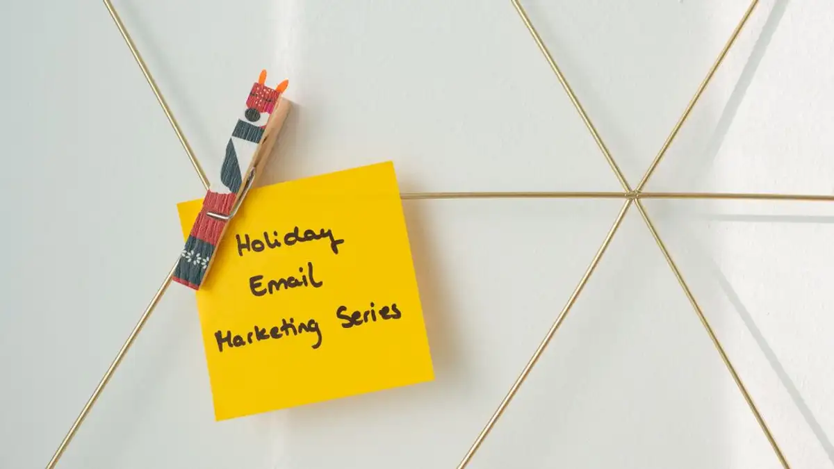 Catatan sticky kuning cerah dengan pesan pemasaran email liburan yang dijepit ke dinding kerangka.