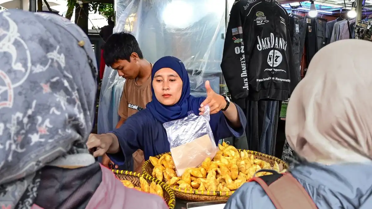 Seorang wanita menjual kue-kue di sebuah kios pasar terbuka pada siang hari.