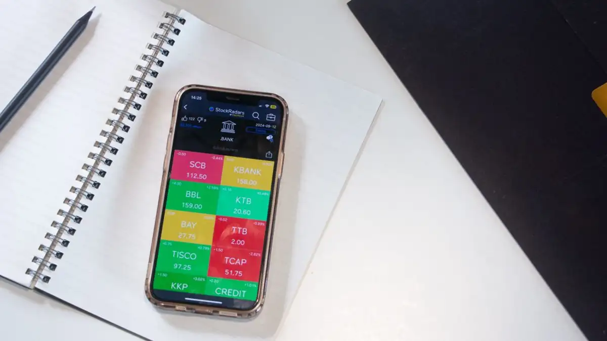 Sebuah smartphone menampilkan aplikasi pasar saham keuangan di atas meja dengan notebook dan pensil.