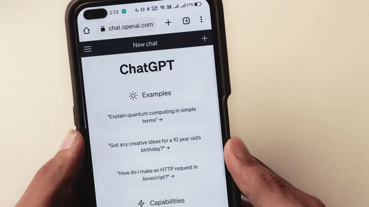 Close-up tangan memegang smartphone yang menampilkan antarmuka aplikasi ChatGPT di layar.