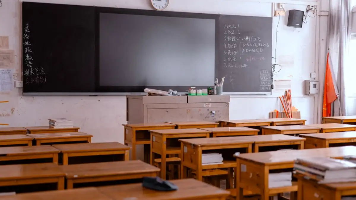 Ruang kelas kosong dengan meja kayu dan papan tulis, menampilkan bahan edukatif.