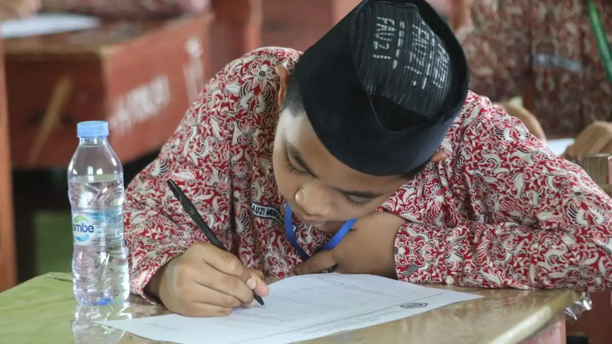 Seorang siswa dengan pakaian tradisional yang fokus menulis ujian di sekolah.