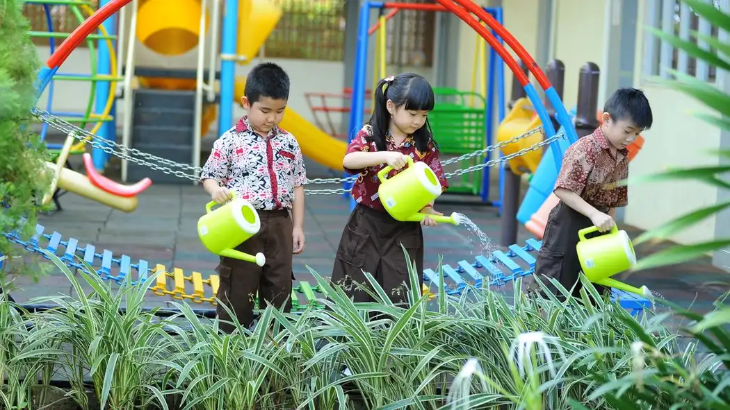 Anak-anak kecil belajar keterampilan berkebun dengan menyiram tanaman di lingkungan taman bermain sekolah yang cerah.